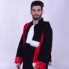Un homme avec une barbe et des cheveux coiffés porte la « Tenue Doctorale de cérémonie », qui se compose d'une robe noire avec des accents rouges et une bordure en fourrure blanche. Il porte également un vêtement blanc semblable à une écharpe autour du cou. Il se tient debout sur un fond uni de couleur claire.