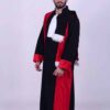 Un homme barbu aux cheveux courts porte la tenue doctorale de cérémonie, qui se compose d'une robe noire avec des touches de rouge et une bordure en fourrure blanche. Il se tient debout sur un fond uni et clair, regardant directement la caméra. La robe a une apparence formelle renforcée par son col blanc.